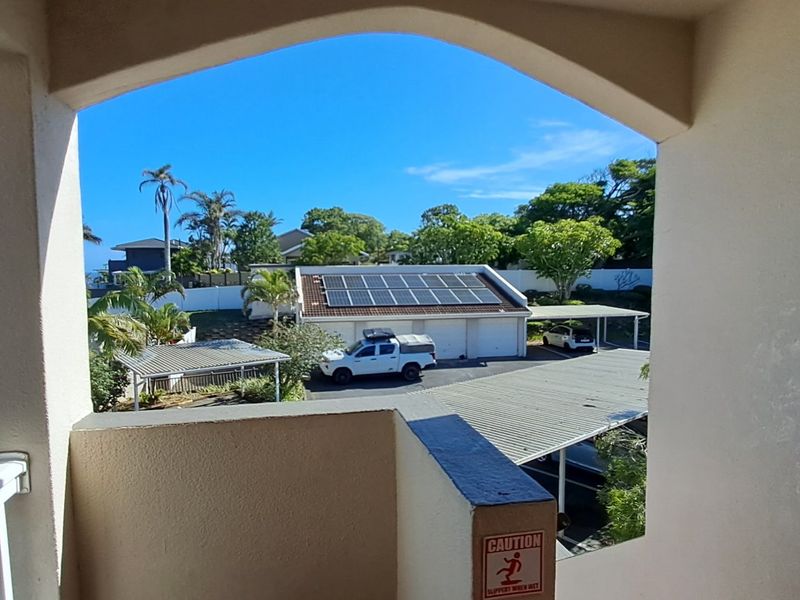 A view from a covered balcony overlooking a residential parking area with carports and solar panels on the roof.