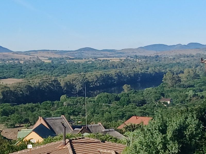 A scenic elevated view overlooking lush green landscape, river, and distant rolling hills.