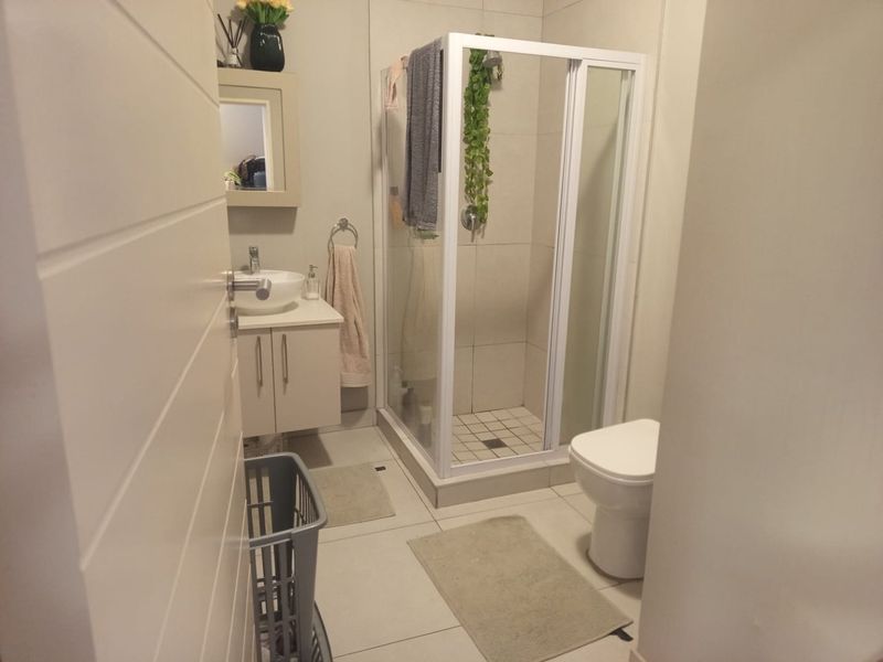 A functional bathroom featuring a shower enclosure, vanity cabinet with vessel sink, and a toilet, finished with neutral wall and floor tiles.