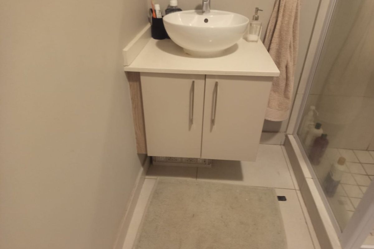 A compact bathroom featuring a modern vessel sink mounted on a white vanity cabinet, adjacent to a glass-enclosed shower with tiled flooring.