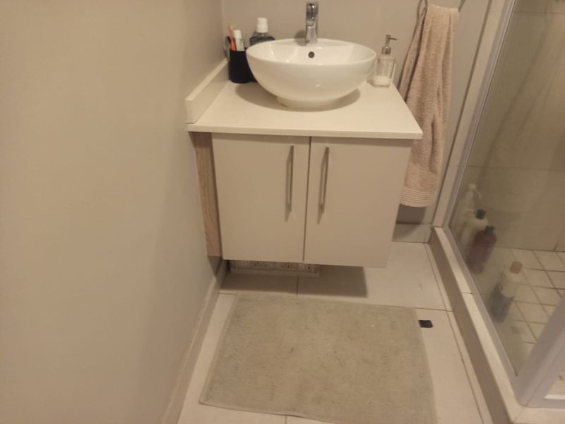 A compact bathroom featuring a modern vessel sink mounted on a white vanity cabinet, adjacent to a glass-enclosed shower with tiled flooring.