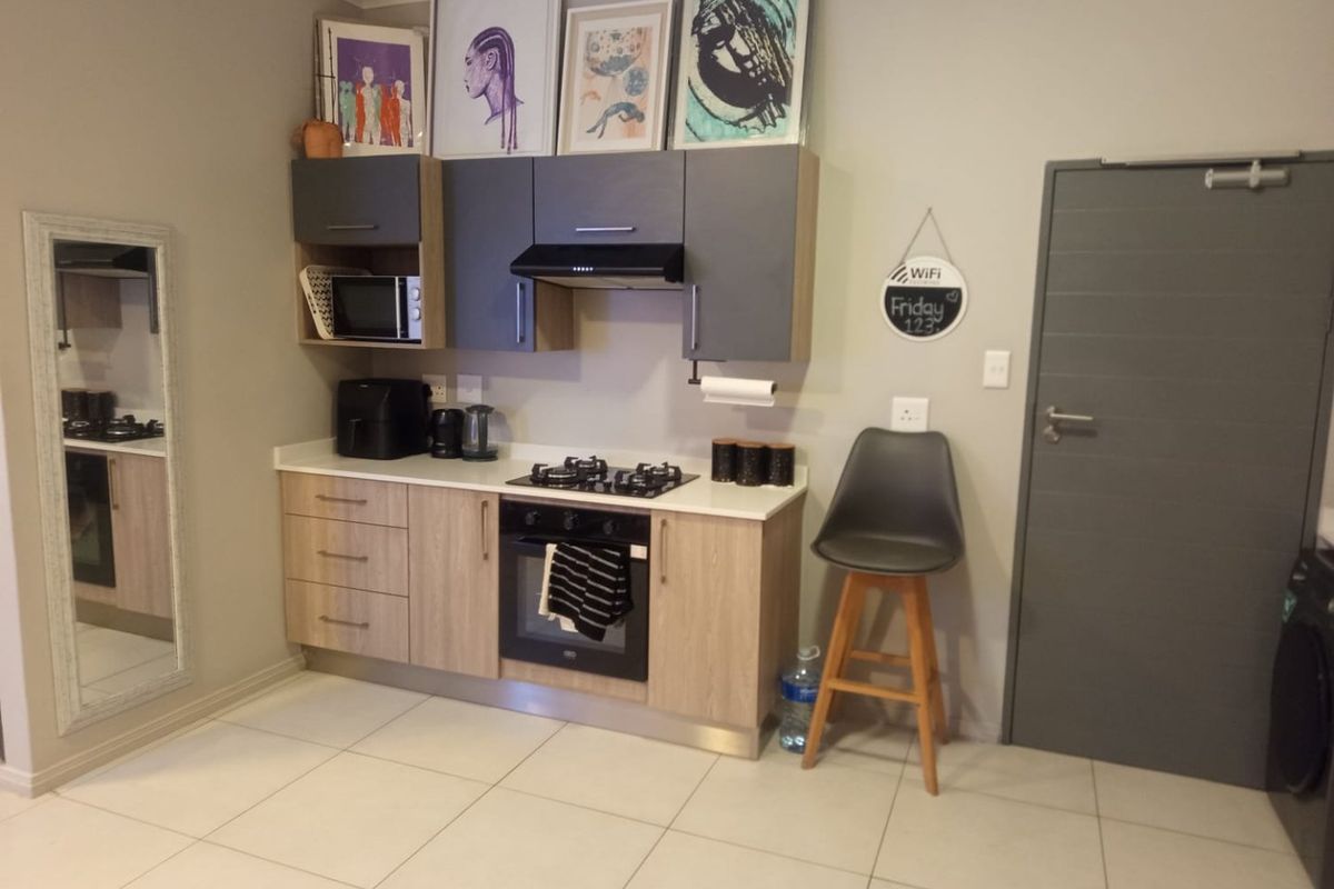 A compact, modern kitchen featuring two-tone cabinetry, a gas hob, built-in oven, extractor fan, and light-colored tiled flooring.