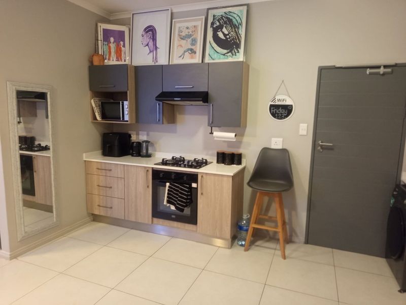 A compact, modern kitchen featuring two-tone cabinetry, a gas hob, built-in oven, extractor fan, and light-colored tiled flooring.