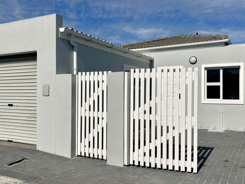 Front exterior view of the property featuring a roller garage door, white picket gate, and paved driveway area.