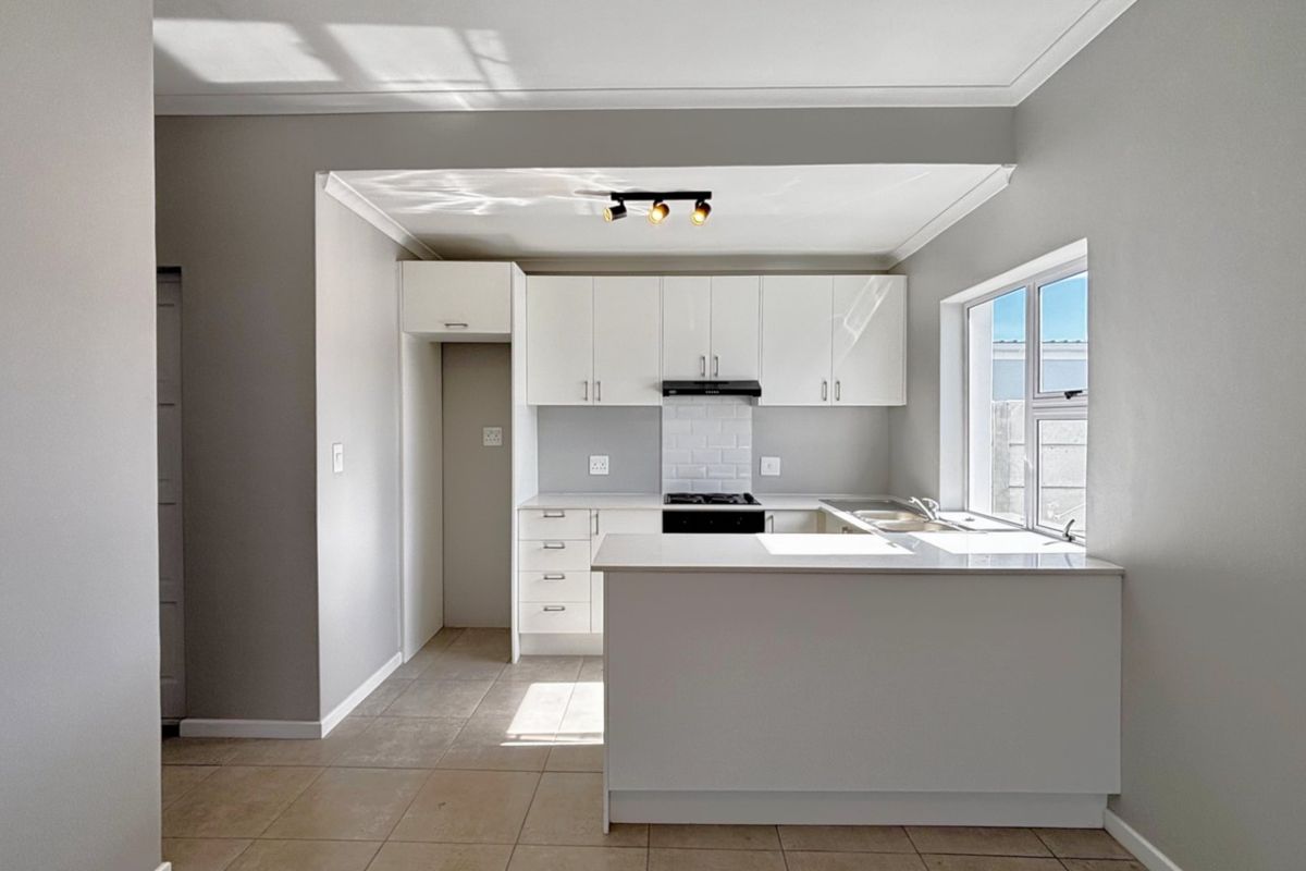 A clean, modern kitchen featuring white cabinetry, stone countertops, a subway tile backsplash, and integrated hob with extractor fan.
