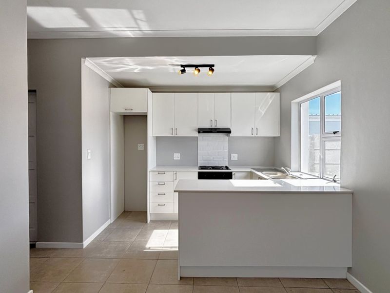 A clean, modern kitchen featuring white cabinetry, stone countertops, a subway tile backsplash, and integrated hob with extractor fan.