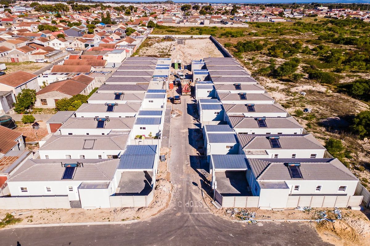 Aerial view of a residential development featuring multiple semi-detached units with tiled roofs, solar water heaters, and private boundary walls under construction.