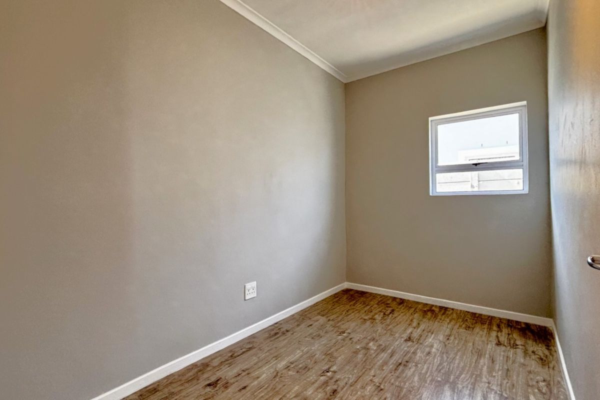 A clean, empty bedroom featuring neutral wall paint, laminate flooring, and a small window, providing a blank canvas for personalization.