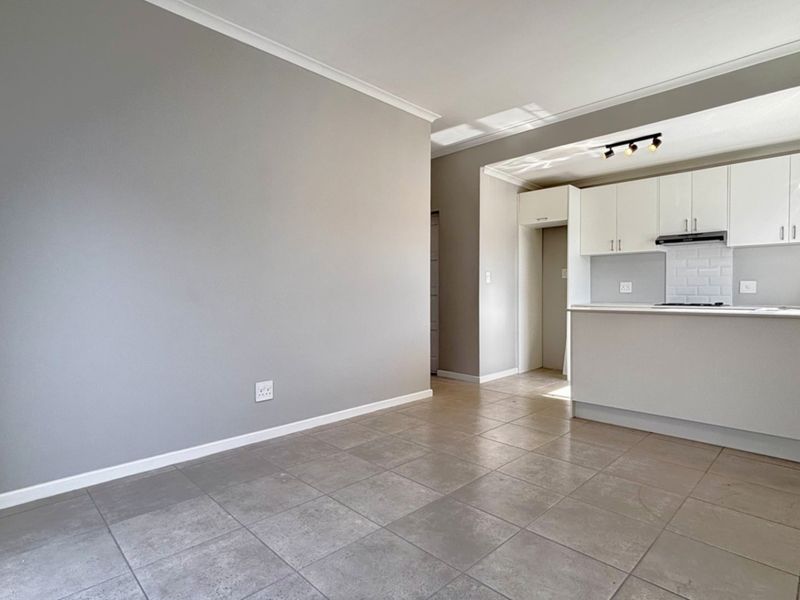 An open-plan living and kitchen area featuring neutral grey walls, tiled flooring, and modern white cabinetry with a subway tile backsplash.
