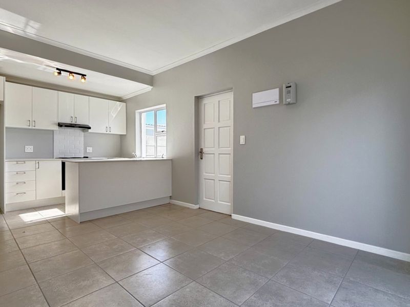 An open-plan living and kitchen area featuring modern white cabinetry, tiled flooring, and a functional kitchen island in a well-maintained space.