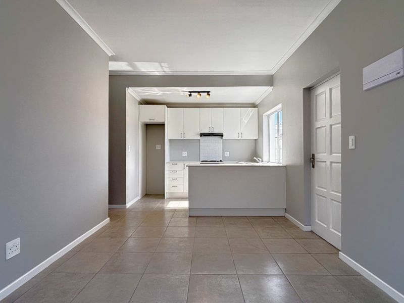 An open-plan living and kitchen area featuring neutral grey walls, tiled flooring, and a modern kitchen with white cabinetry and a subway tile backsplash.