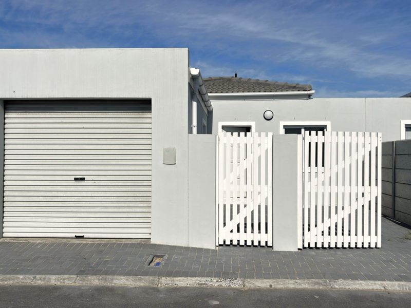 Front exterior view of the property featuring a secure roller garage door, white picket pedestrian gate, and paved driveway access.