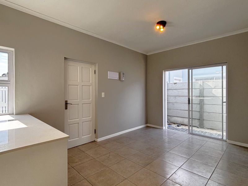 A bright, empty kitchen area featuring tiled flooring, a stone countertop, and direct access to an outdoor space via a sliding glass door.