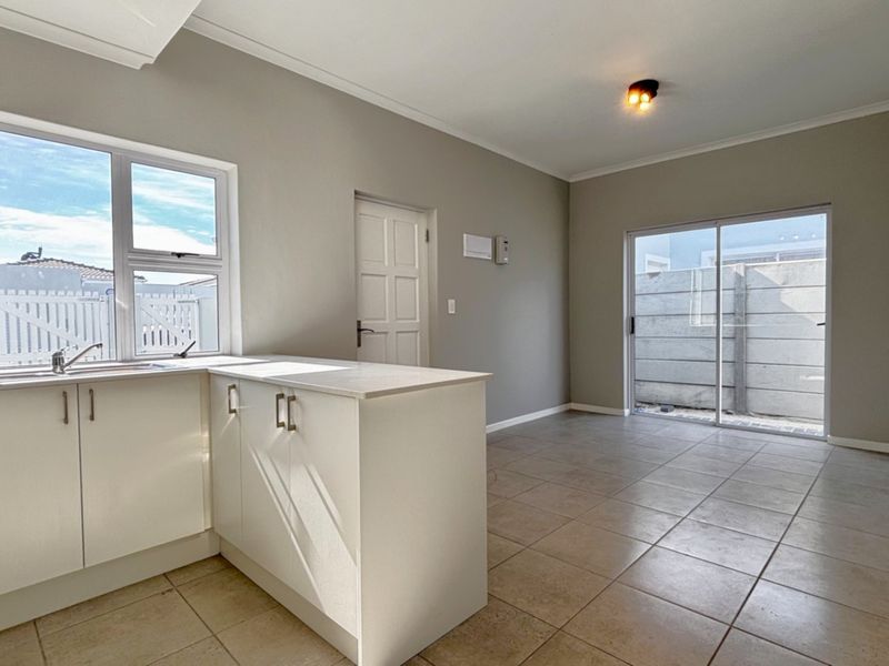 An open-plan kitchen and living area featuring neutral walls, tiled flooring, and direct access to an outdoor space through a sliding glass door.