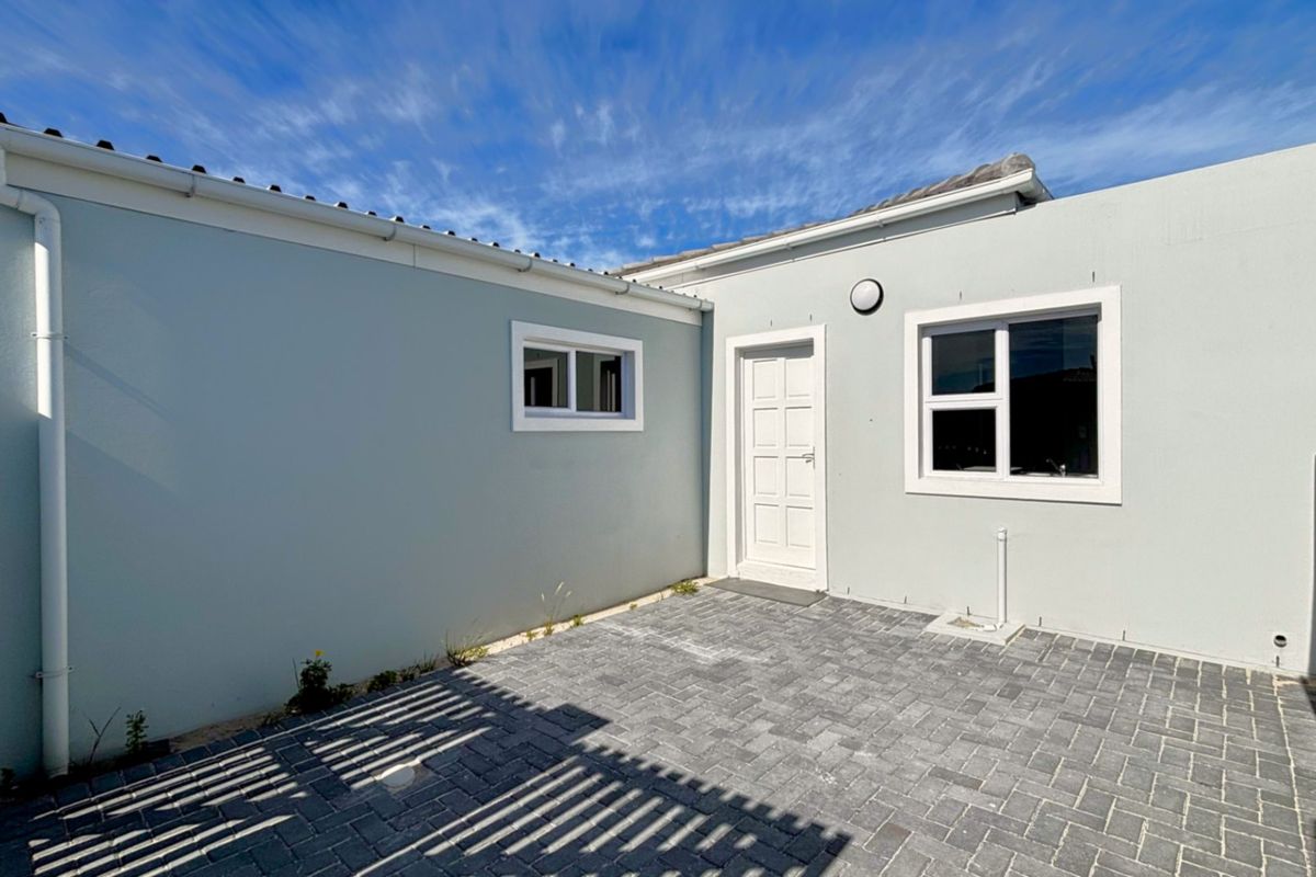 A clean and well-maintained rear courtyard featuring paved flooring, external lighting, and secure boundary walls.