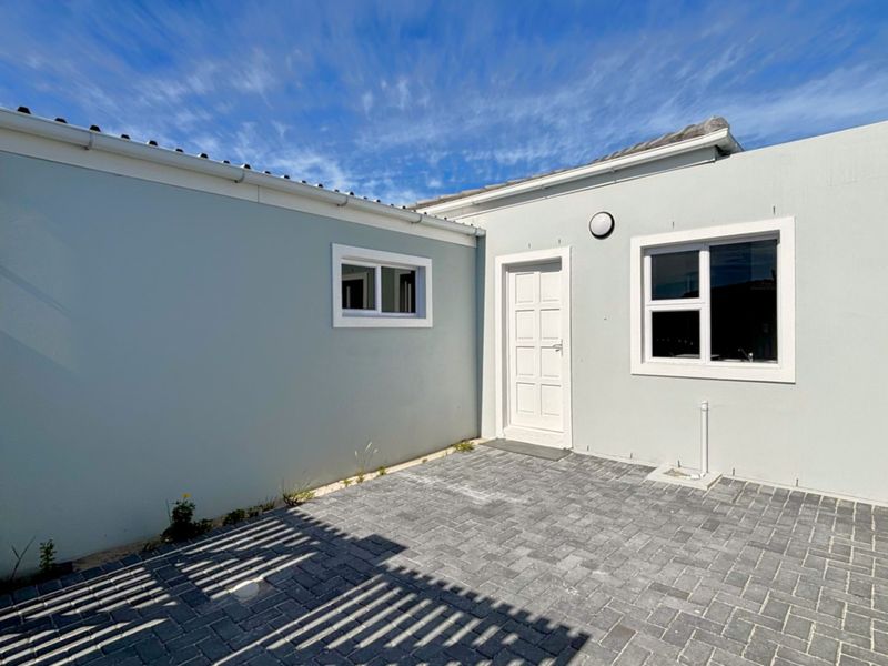 A clean and well-maintained rear courtyard featuring paved flooring, external lighting, and secure boundary walls.