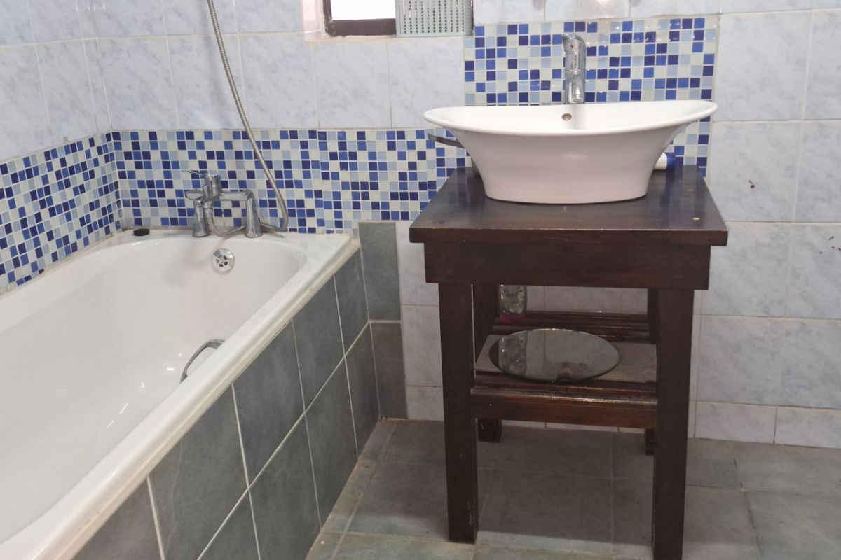 A dated bathroom featuring a bathtub, vessel sink on a wooden vanity, and blue mosaic tile accents.