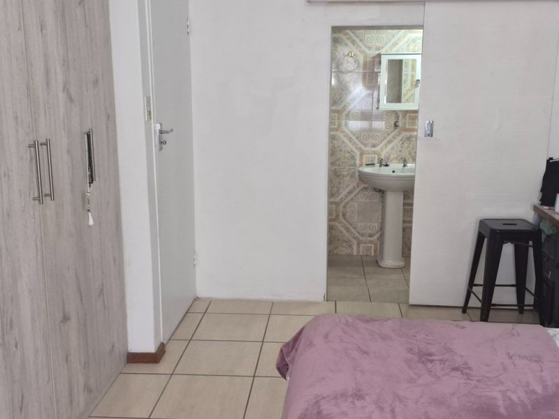 A bedroom featuring built-in cupboards, tiled flooring, and an en-suite bathroom with a pedestal basin.