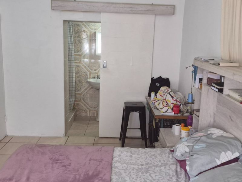 A bedroom featuring tiled flooring, a built-in wardrobe, and direct access to an en-suite bathroom with a pedestal basin and shower.