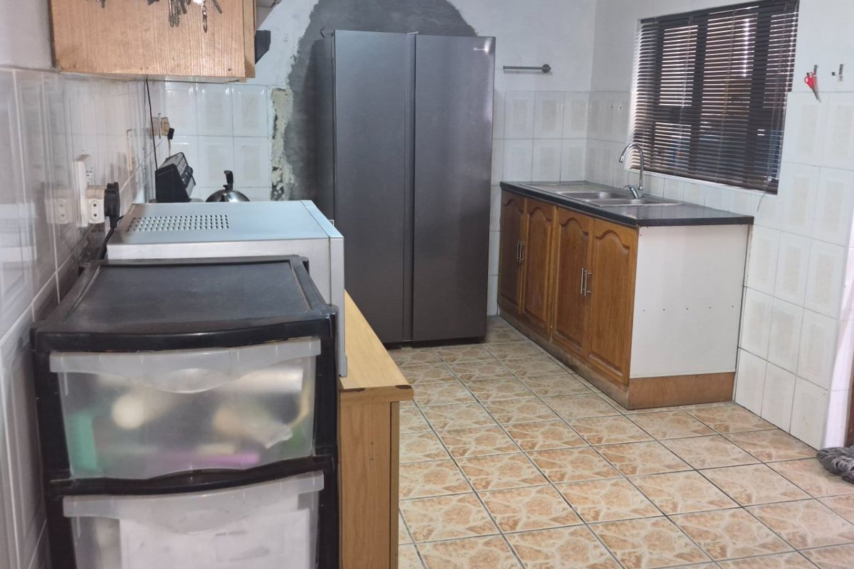 A functional kitchen featuring tiled walls and flooring, wooden cabinetry, and a double sink, currently requiring cosmetic updates and wall repairs.