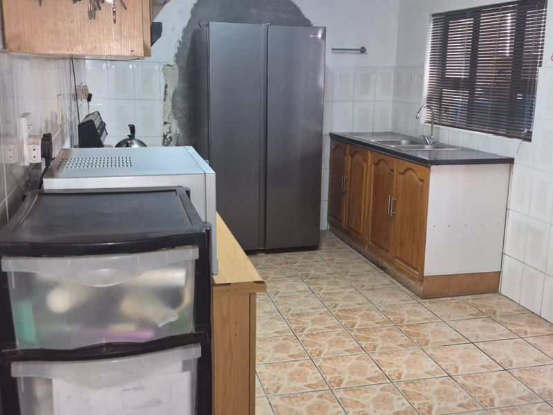 A functional kitchen featuring tiled walls and flooring, wooden cabinetry, and a double sink, currently requiring cosmetic updates and wall repairs.