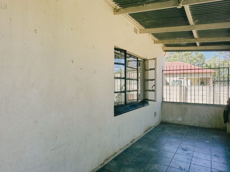 A covered outdoor patio area featuring tiled flooring, steel security bars, and a corrugated metal roof, requiring some maintenance and cosmetic updates.