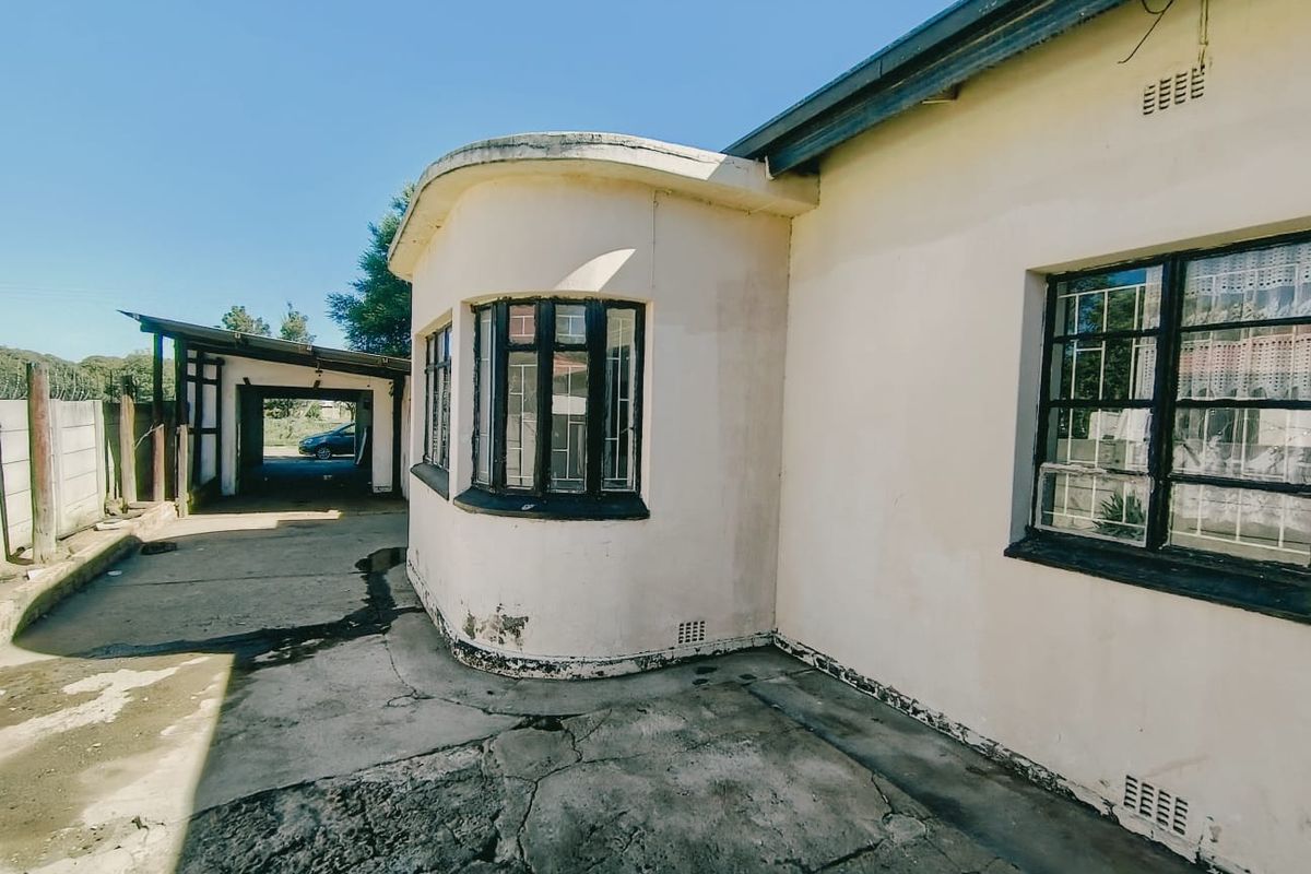 Rear exterior view of the property featuring a distinctive curved bay window, security bars, and a concrete driveway leading to a carport.
