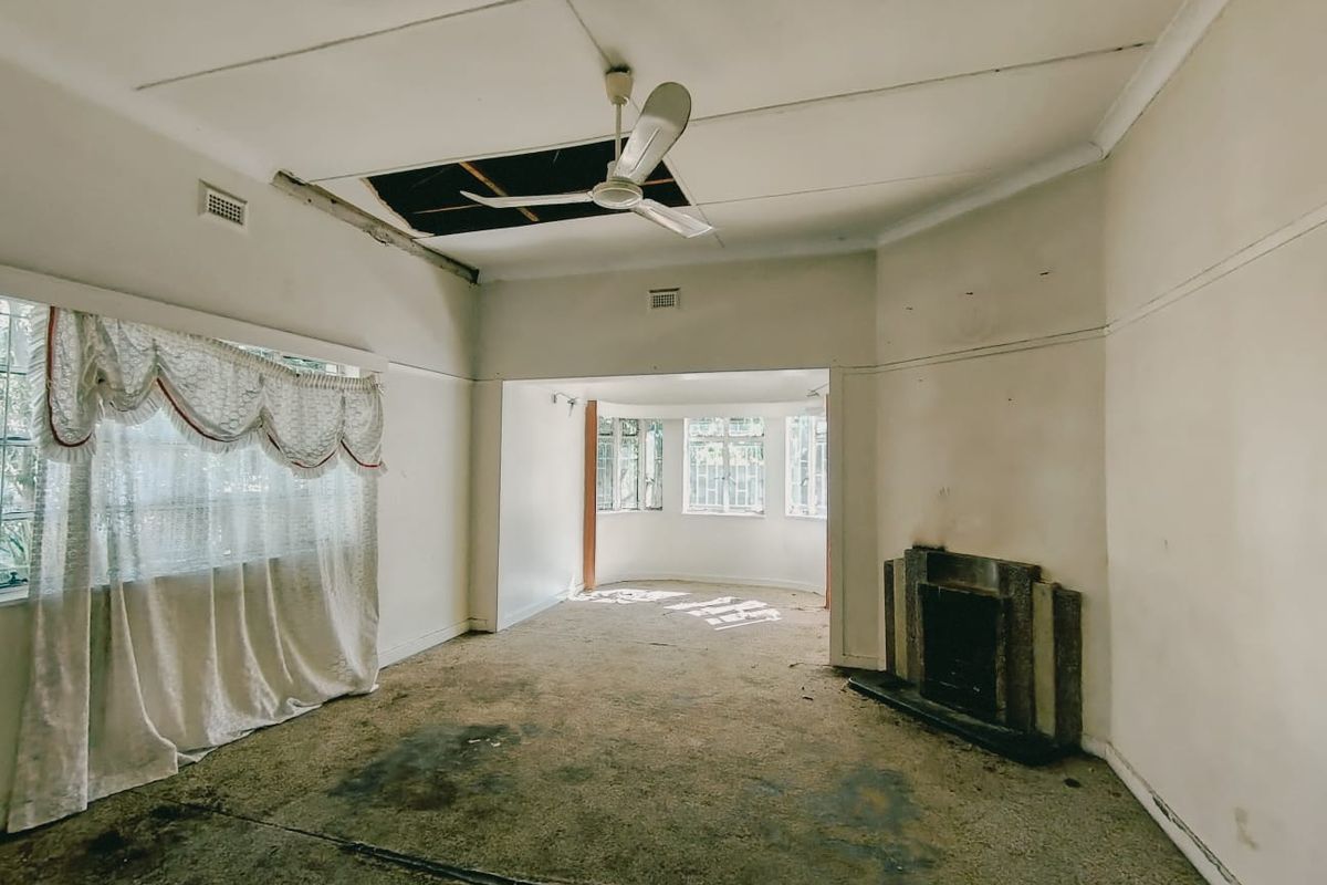 Spacious living area featuring a fireplace and large windows, currently in need of significant renovation and repair to the ceiling and flooring.