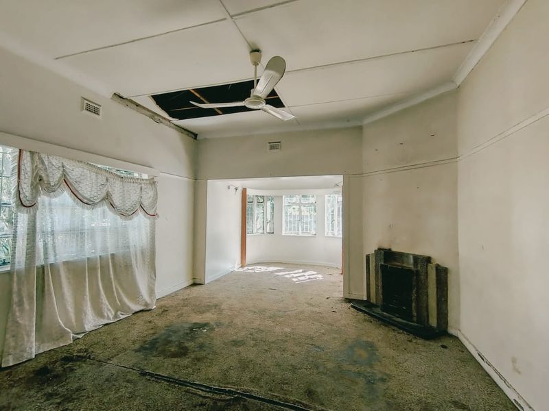 Spacious living area featuring a fireplace and large windows, currently in need of significant renovation and repair to the ceiling and flooring.