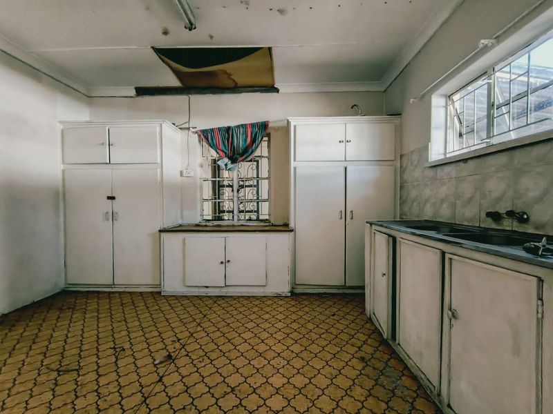 A dated kitchen featuring built-in cabinetry, a sink, and tiled flooring, currently in need of significant renovation and ceiling repairs.