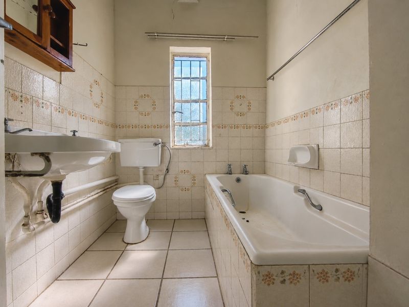 A dated bathroom featuring a pedestal basin, toilet, and bathtub with original ceramic tiling, requiring modernization and cosmetic updates.