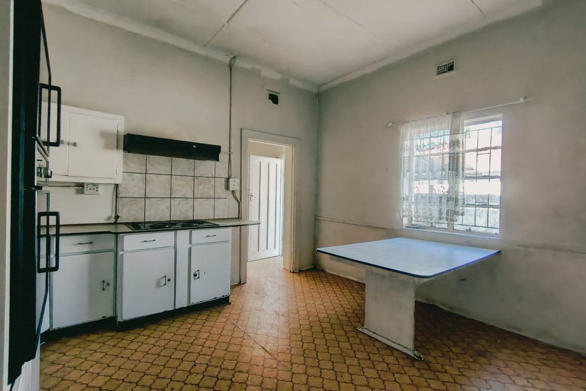A dated kitchen featuring original cabinetry, a built-in hob, and a fixed breakfast table, requiring renovation to modernize the space.