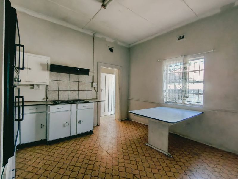 A dated kitchen featuring original cabinetry, a built-in hob, and a fixed breakfast table, requiring renovation to modernize the space.