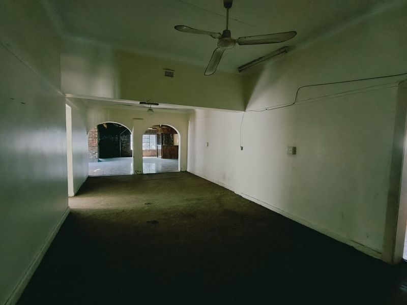 An empty, dated living area featuring archways, ceiling fans, and worn carpeting, requiring significant cosmetic updates and repairs to electrical finishes.