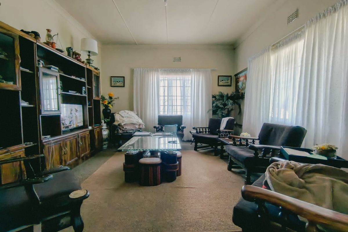 A spacious living room featuring a large built-in wooden shelving unit and windows fitted with security bars, offering a traditional layout.