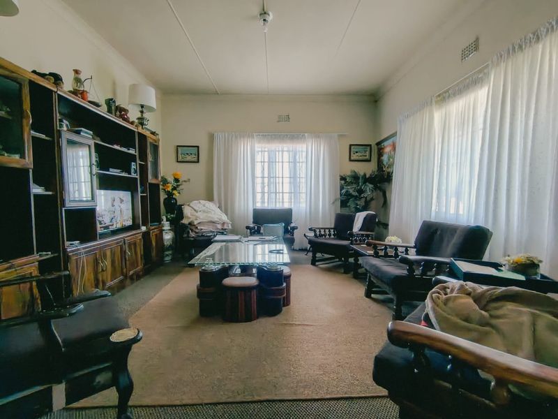 A spacious living room featuring a large built-in wooden shelving unit and windows fitted with security bars, offering a traditional layout.