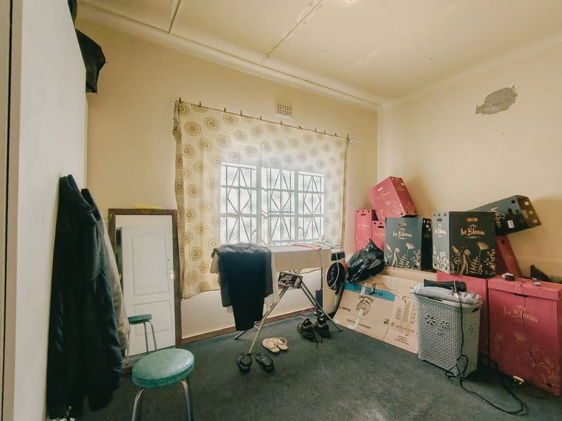 A bedroom space featuring a security gate on the window and built-in cupboard, currently used for storage with visible wear to walls and flooring.