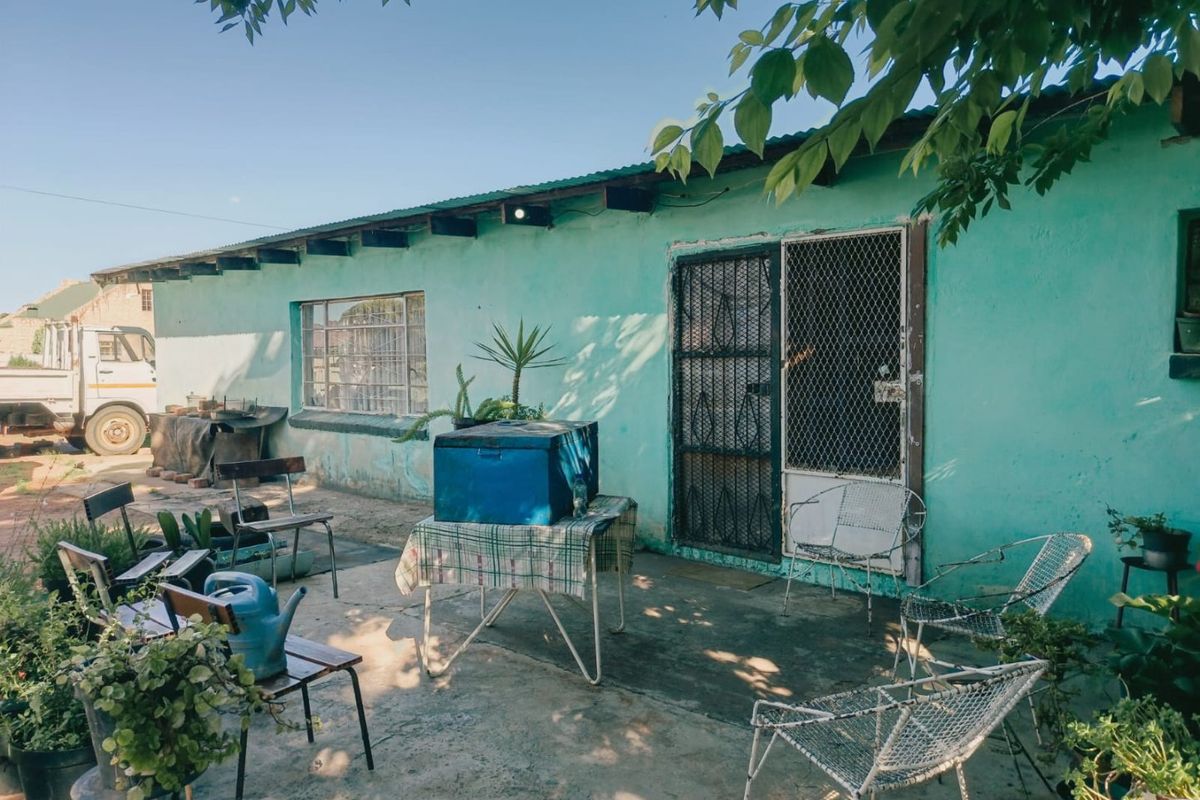 Rear exterior view of the house featuring a concrete patio area, security gate, and painted masonry walls showing signs of wear.
