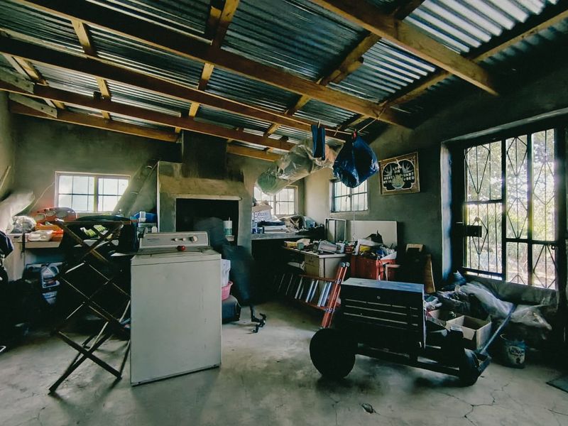 A utility space featuring exposed timber roof trusses, a corrugated metal roof, a built-in fireplace, and concrete flooring with security gate access.