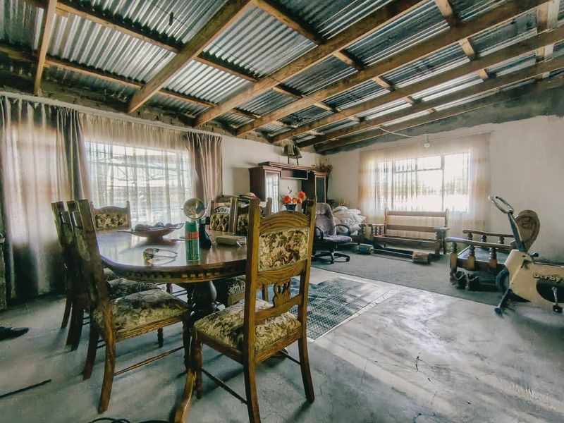 Spacious living area featuring exposed timber roof trusses, corrugated metal ceiling, and concrete flooring, offering a rustic, industrial-style foundation for renovation.