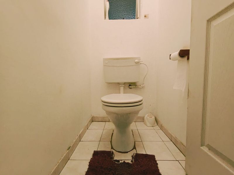 A compact, functional guest toilet featuring tiled flooring and a small obscured glass window for natural light.