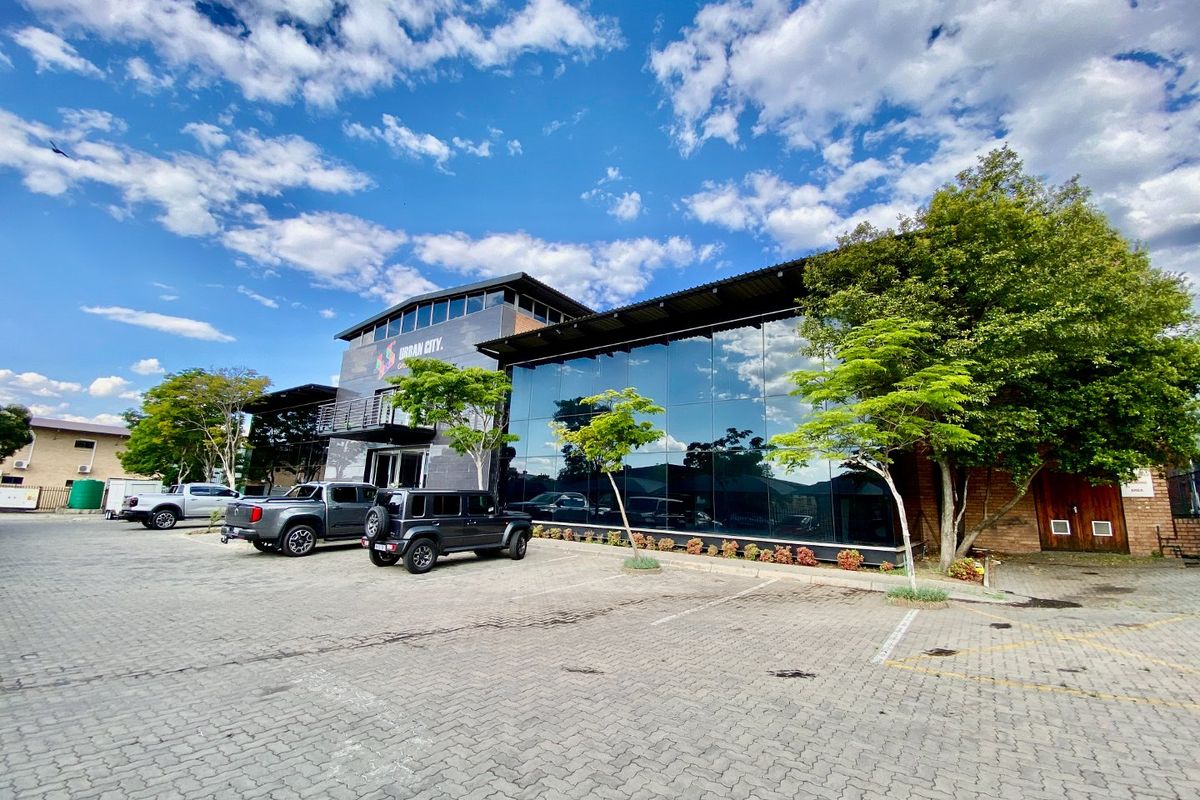 Modern industrial commercial building featuring a prominent glass curtain wall facade, paved parking area, and contemporary architectural design.