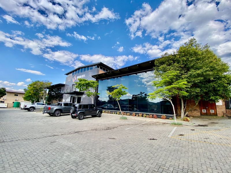 Modern industrial commercial building featuring a prominent glass curtain wall facade, paved parking area, and contemporary architectural design.
