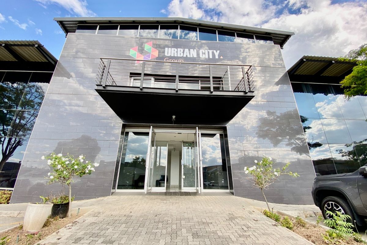 Modern industrial office building facade featuring dark tiled cladding, glass curtain walls, and a prominent entrance with a metal balcony.
