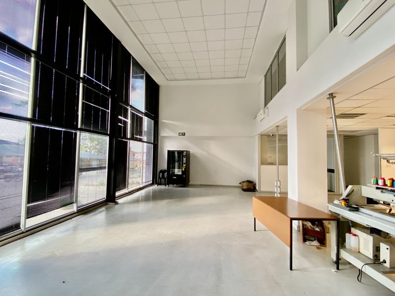 Spacious open-plan industrial office area featuring high ceilings, large windows providing ample natural light, polished concrete floors, and integrated air conditioning units.