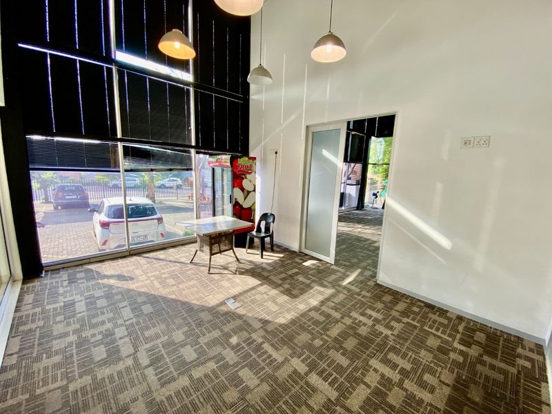 A bright, open-plan office space featuring large floor-to-ceiling windows, carpeted flooring, and modern recessed lighting, offering a professional and airy work environment.