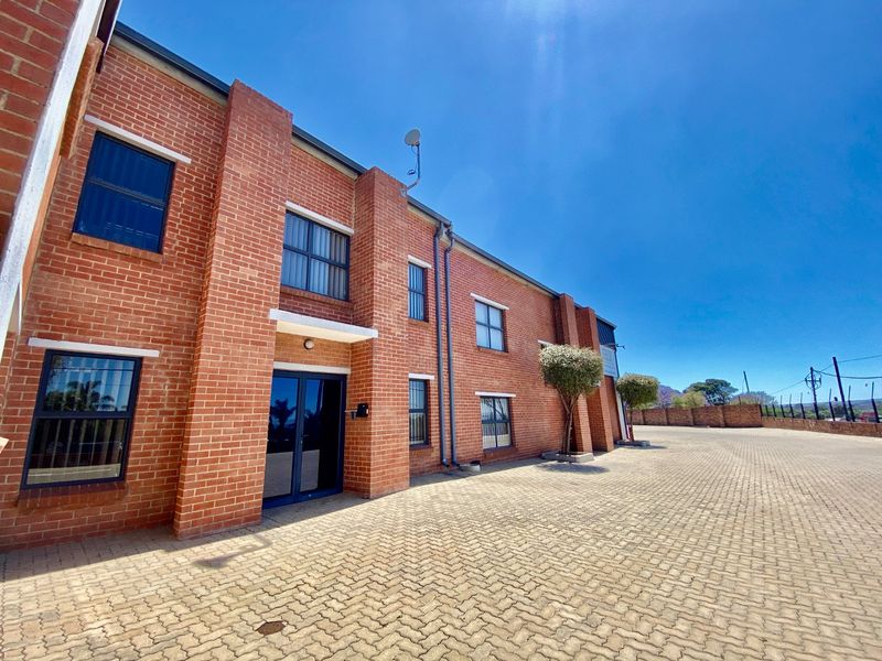 A well-maintained industrial building featuring a face brick facade, paved driveway, and aluminium window frames.