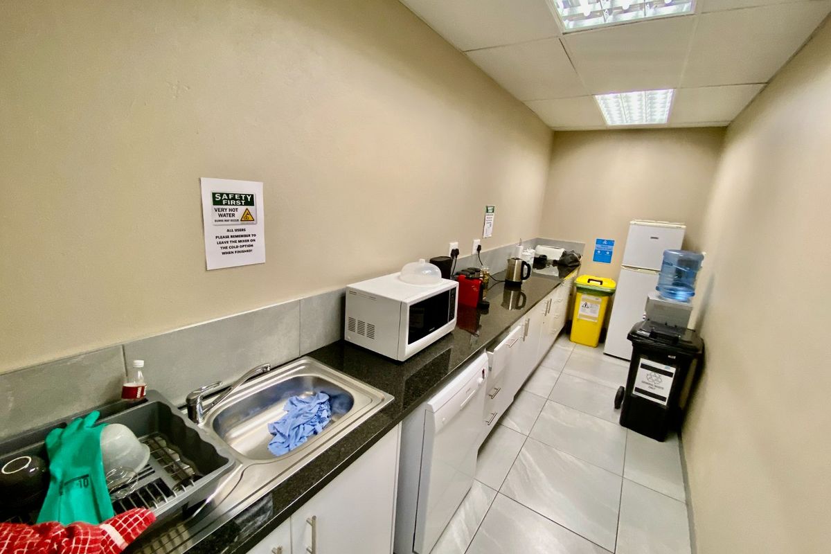 A functional industrial kitchenette featuring granite countertops, stainless steel sink, built-in cabinetry, and tiled flooring, suitable for office or warehouse staff use.