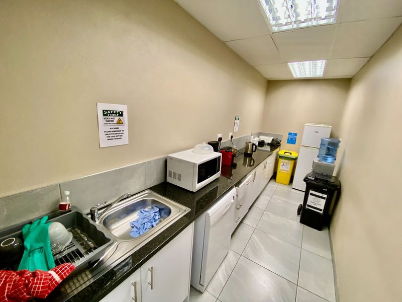 A functional industrial kitchenette featuring granite countertops, stainless steel sink, built-in cabinetry, and tiled flooring, suitable for office or warehouse staff use.