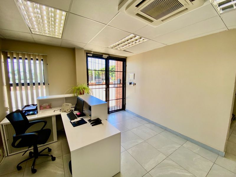 A functional office space featuring tiled flooring, a suspended ceiling with recessed lighting, ducted air conditioning, and a secure entrance door.